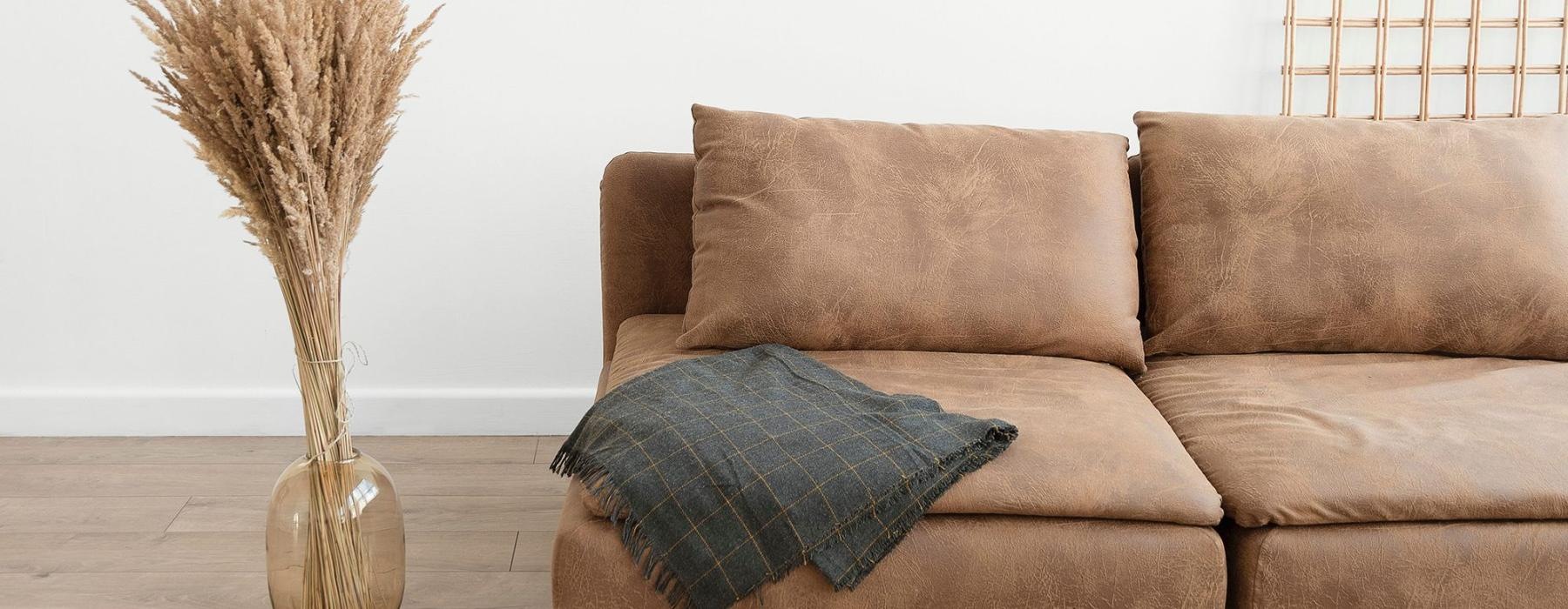 living room with a throw on a couch beside a large floor vase with a plant in it